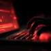 Main d’un homme tapant sur un clavier d’ordinateur avec à l’écran des alertes rouges signalant une cyberattaque.